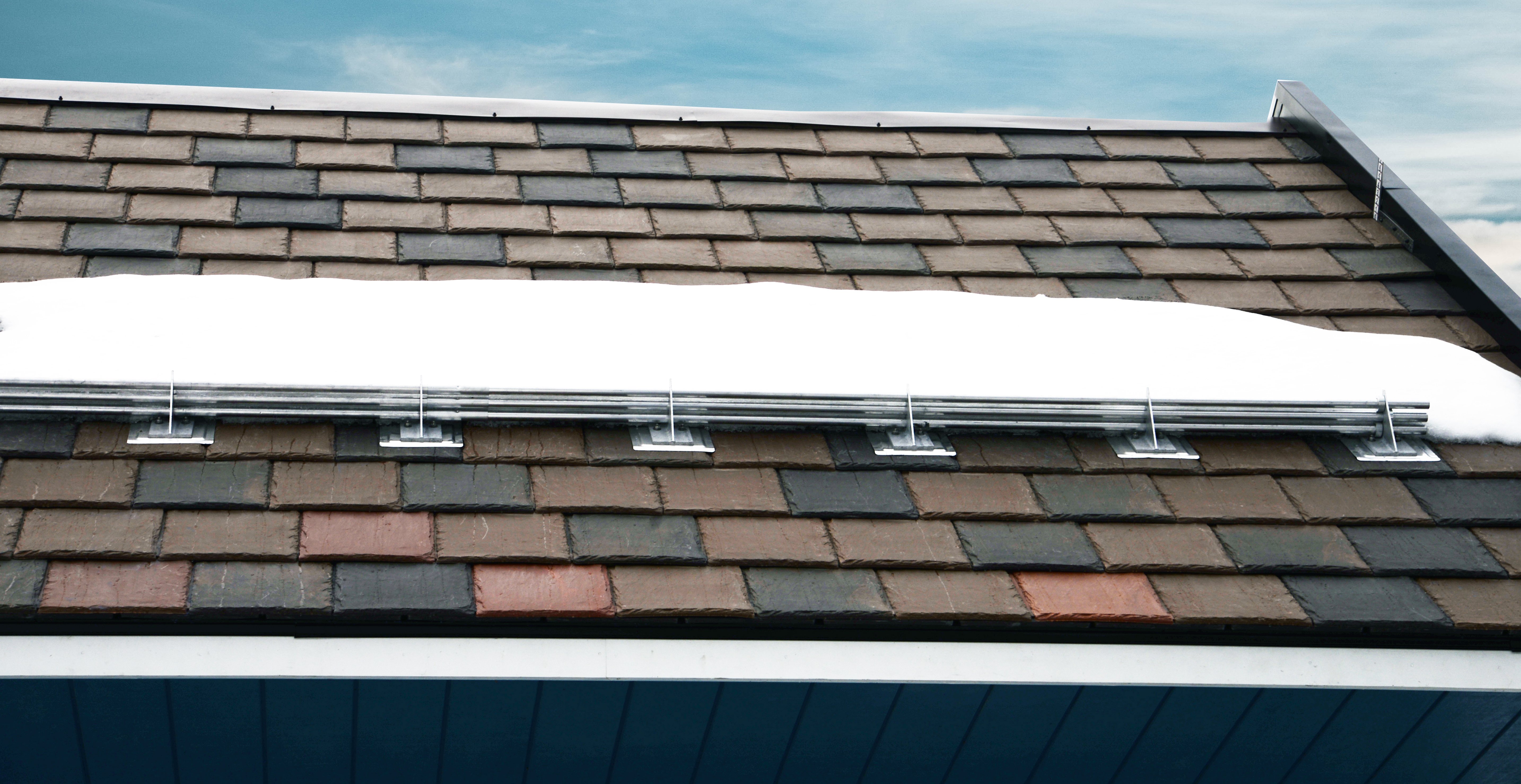 Hybrid pad and pipe style snow guard system for synthetic slate shingle roofing.